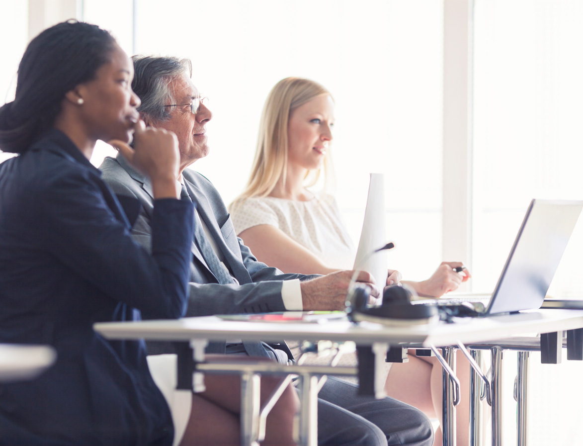 Three Professionals Sitting at a Desk watching a Presentation